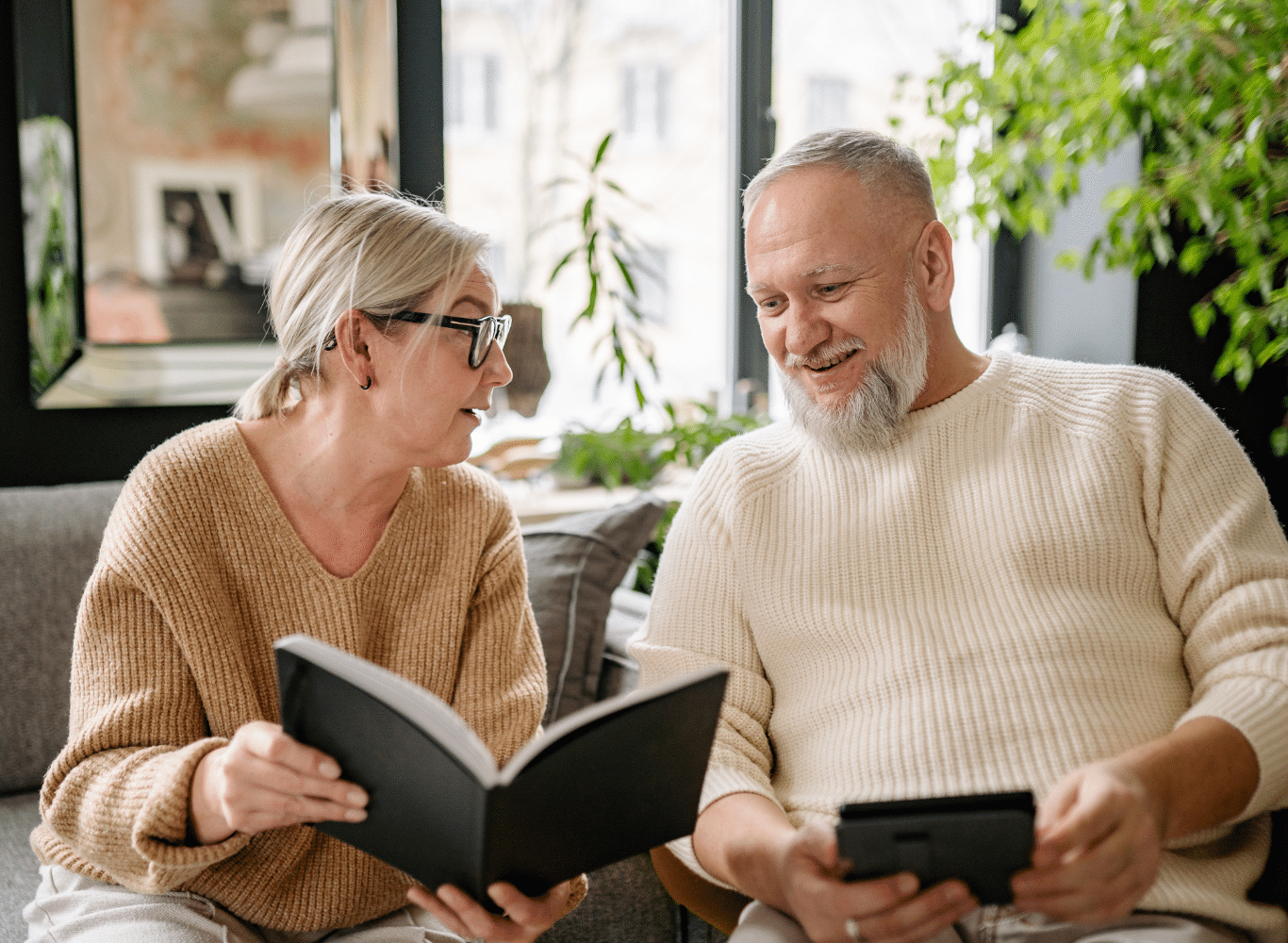 elderly couple on couple smiling at book and tablet